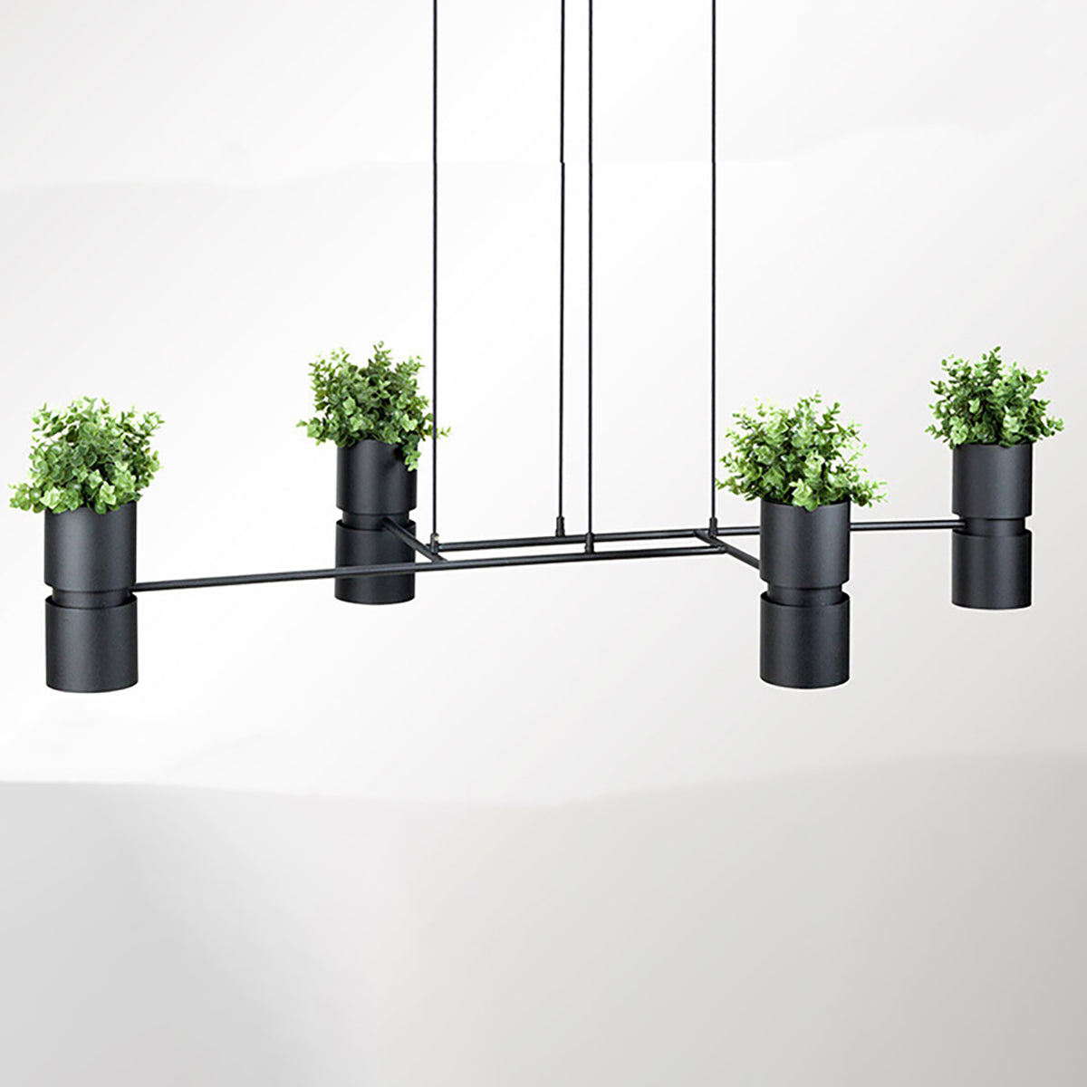 Luminaire suspendu noir à quatre cylindres avec plantes vertes, face, sur fond blanc.