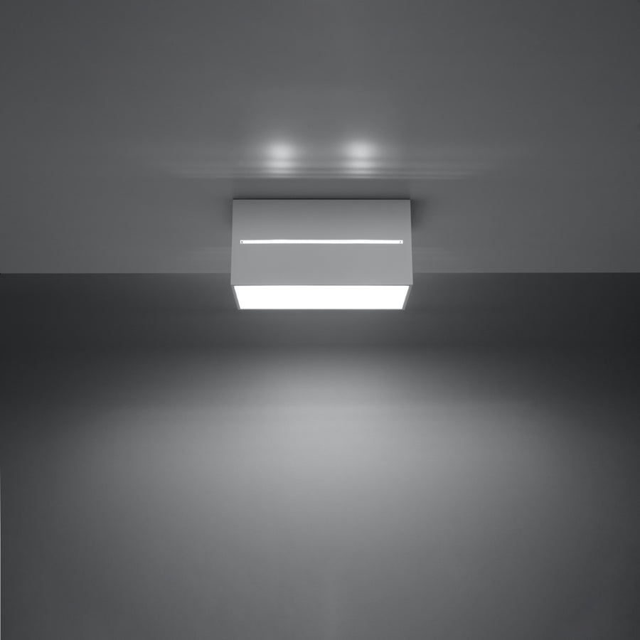 Vue de face du luminaire allumé, éclairant le plafond et diffusant une lumière blanche.