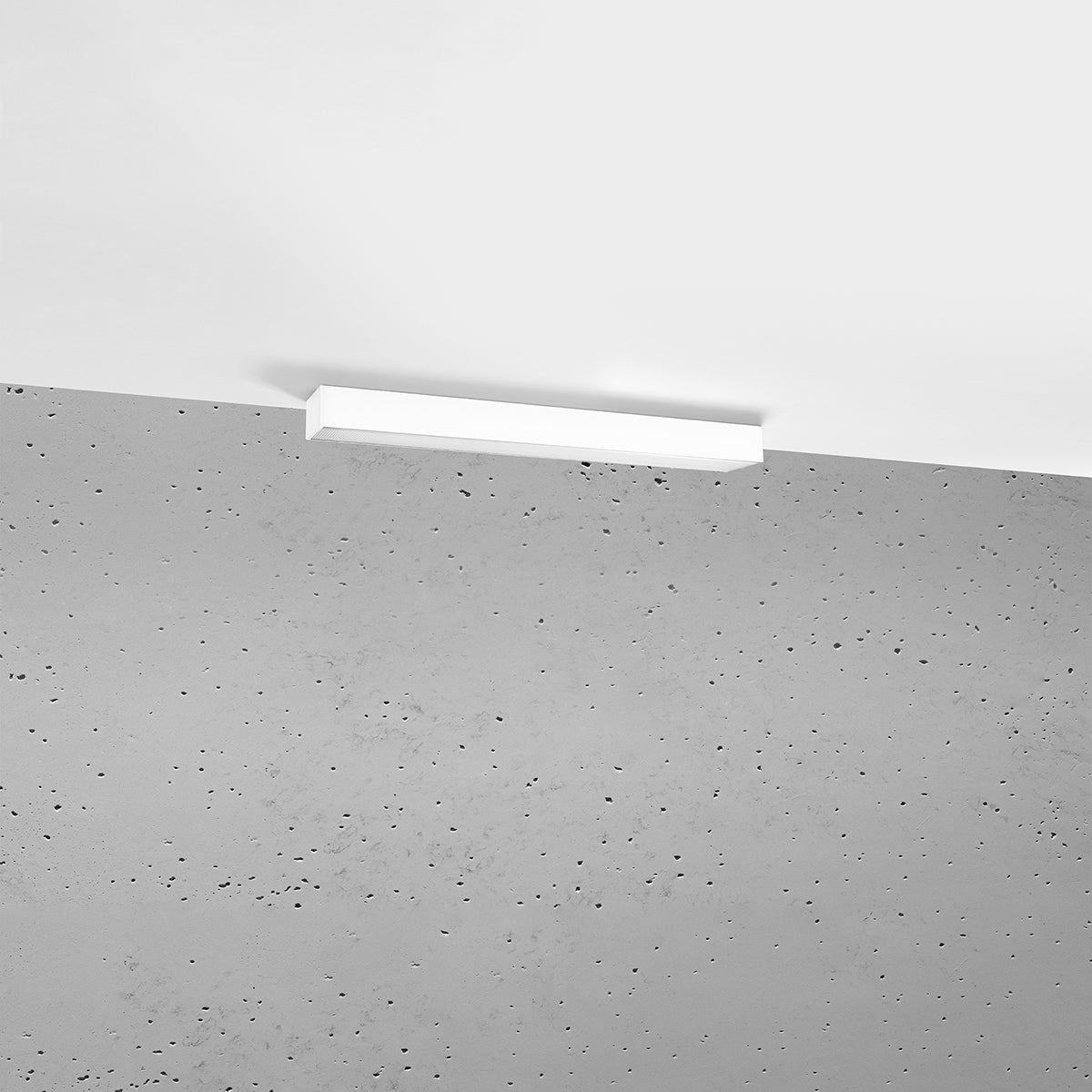 Plafonnier blanc fin fixé au plafond devant un mur en béton brut