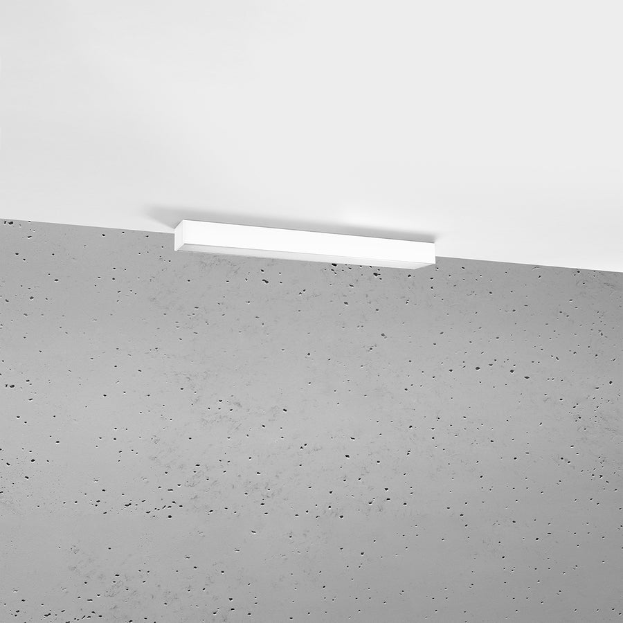 Plafonnier blanc fin fixé au plafond devant un mur en béton brut