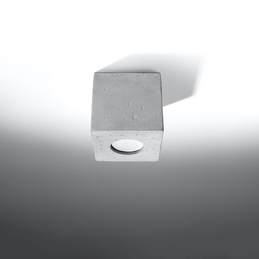 Vue de trois quarts du plafonnier cubique en béton sur fond gris clair.