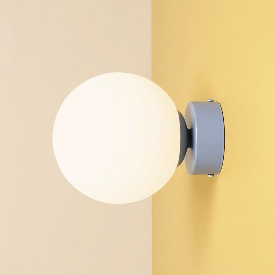 Applique murale au globe blanc lumineux fixé sur un mur jaune pâle.