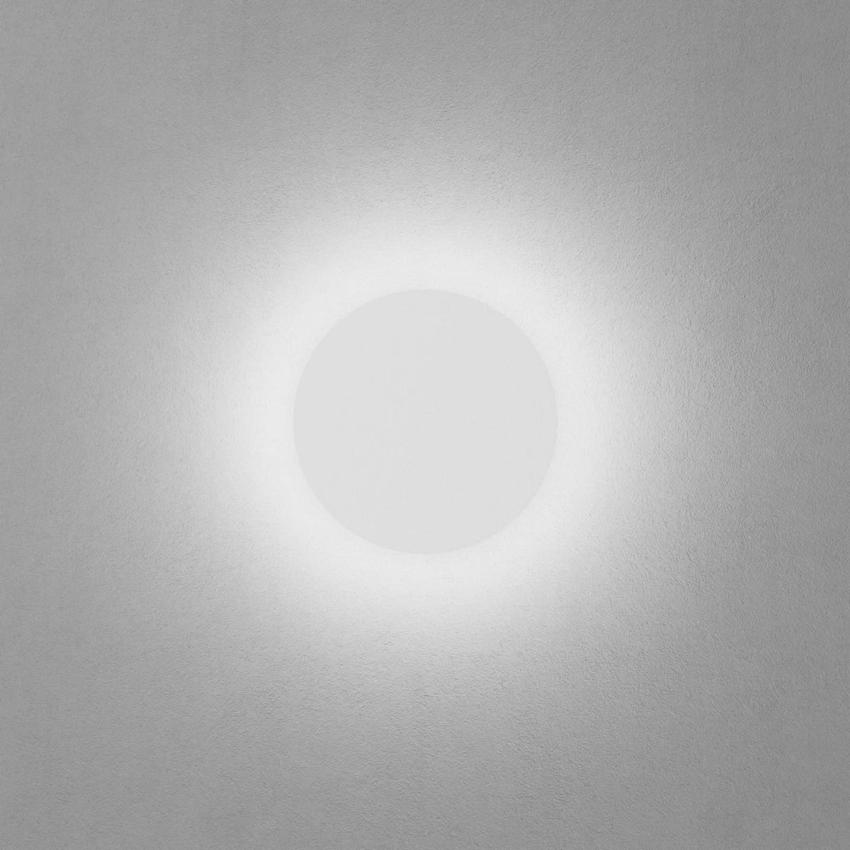 Applique circulaire allumée sur mur gris, lumière blanche en halo