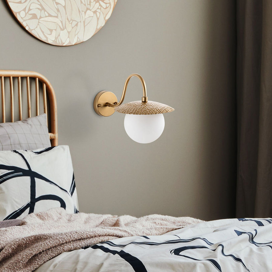 Applique murale dorée installée au-dessus d’un lit dans une chambre