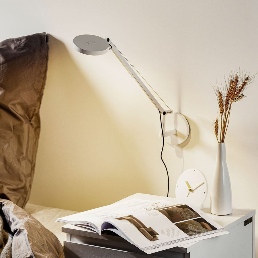 Vue de la lampe au-dessus d’un chevet, avec livre ouvert, horloge et vase.