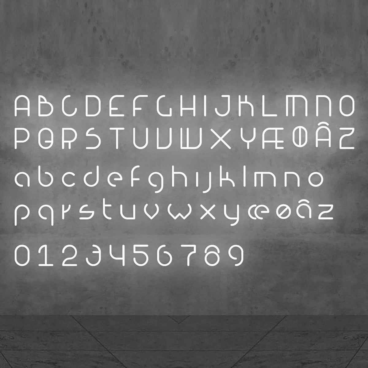 L'alphabet complet et les chiffres stylisés brillent en blanc sur un mur gris.