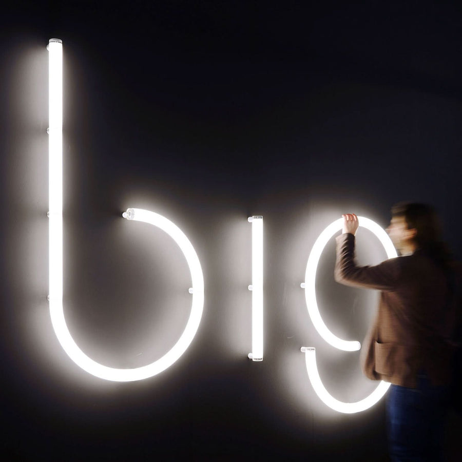 Homme installant une grande lettre lumineuse sur un mur noir.