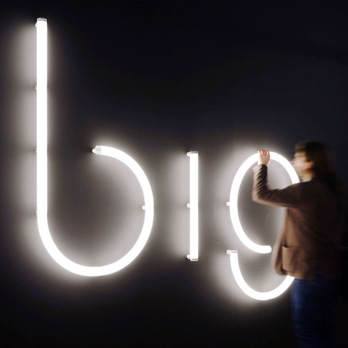 Une personne installe une grande lettre b lumineuse aux côtés d'autres lettres blanches.