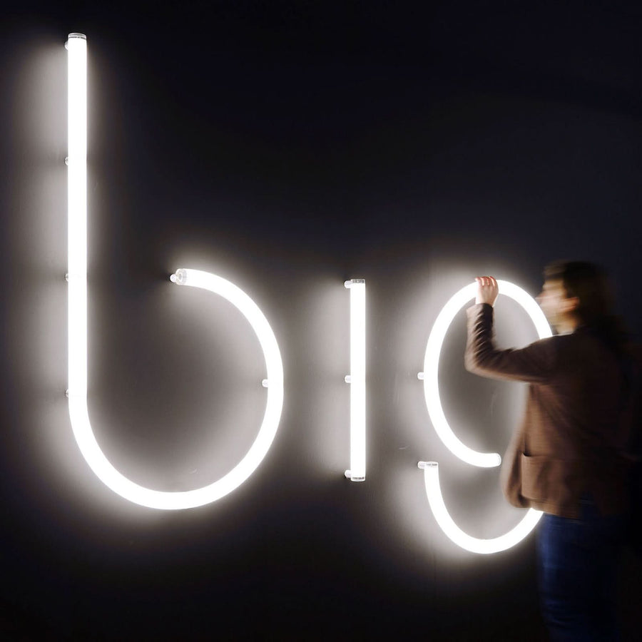 Une personne installe une grande lettre b lumineuse aux côtés d'autres lettres blanches.