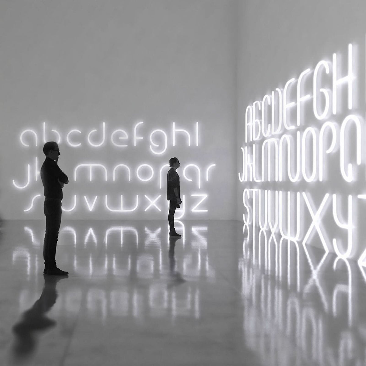 Vue d’ambiance dans une galerie : grandes lettres lumineuses blanches et reflets au sol.