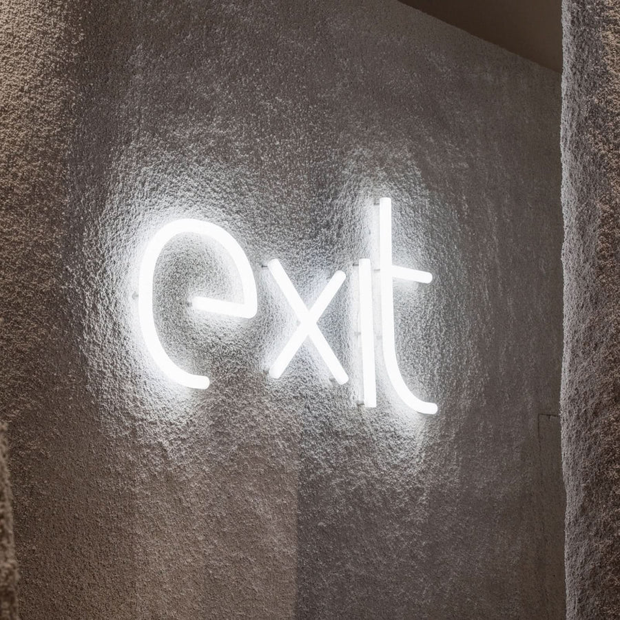 Mot 'exit' en lettres lumineuses blanches fixé sur un mur texturé beige.