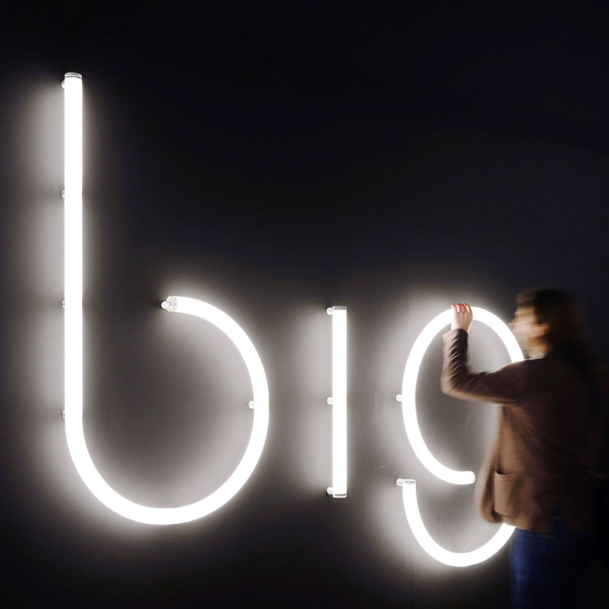 Personne touchant de grandes lettres lumineuses blanches sur un mur noir.