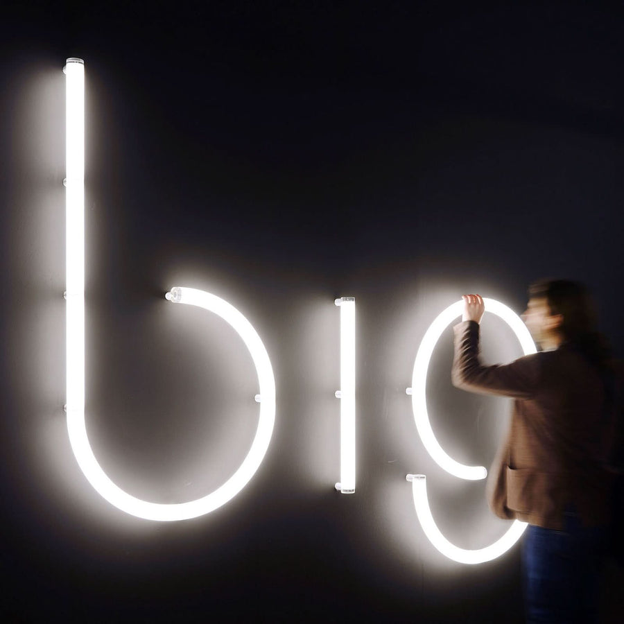 Personne ajustant de grandes lettres lumineuses blanches sur un mur sombre.