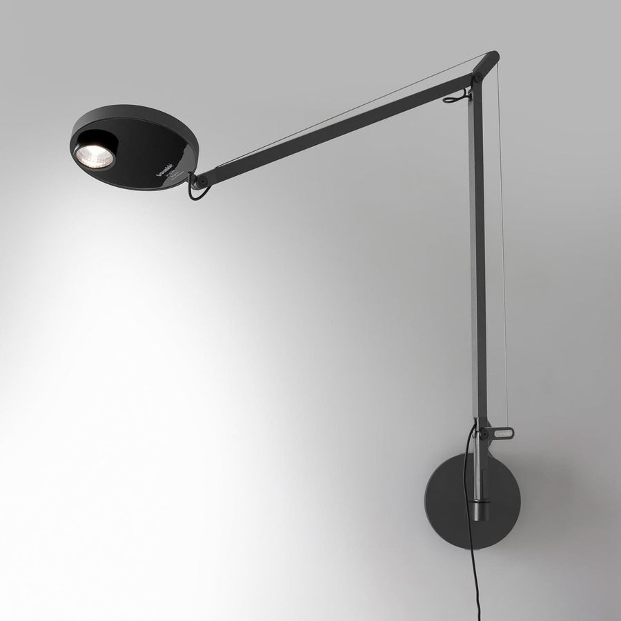 Applique murale anthracite fixée au mur, bras articulé déployé et tête LED allumée.