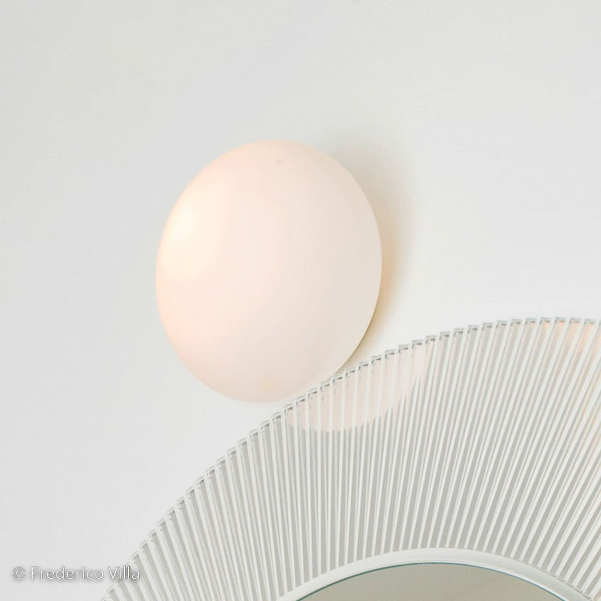 Applique sphérique blanche allumée au-dessus d’un miroir rond à bord de verre strié.