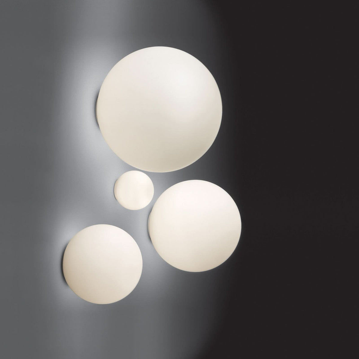 Quatre globes lumineux blancs de tailles différentes sur fond sombre, composition murale.