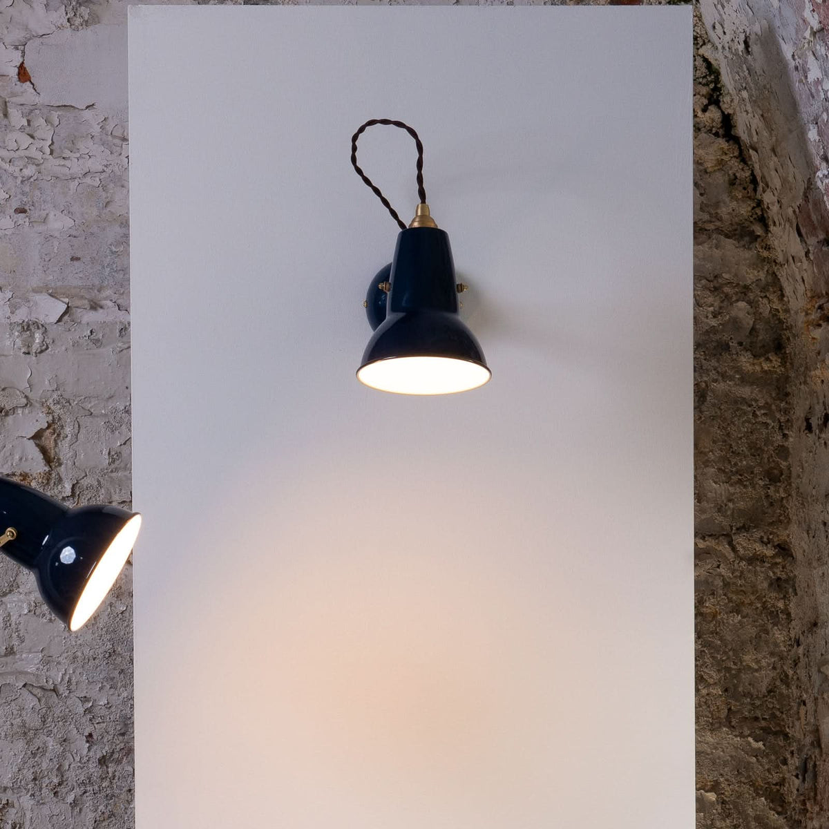 Vue de face de l'applique murale bleu foncé allumée, fixée sur un panneau blanc.