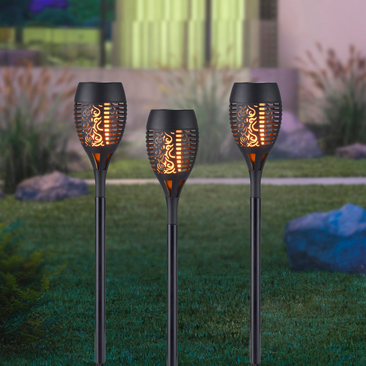 Mise en ambiance nocturne de trois piquets lumineux plantés dans une pelouse.