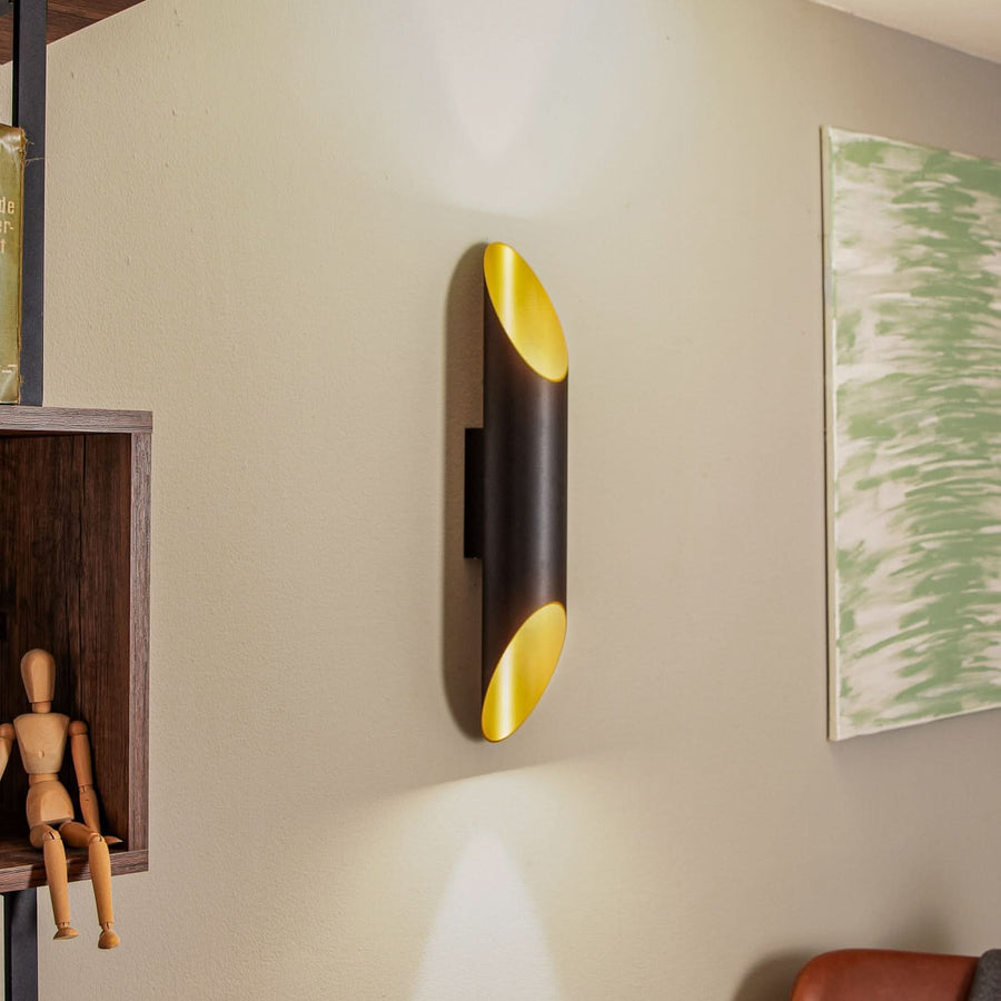 Applique murale noire et dorée installée sur un mur beige, près d'une étagère en bois.