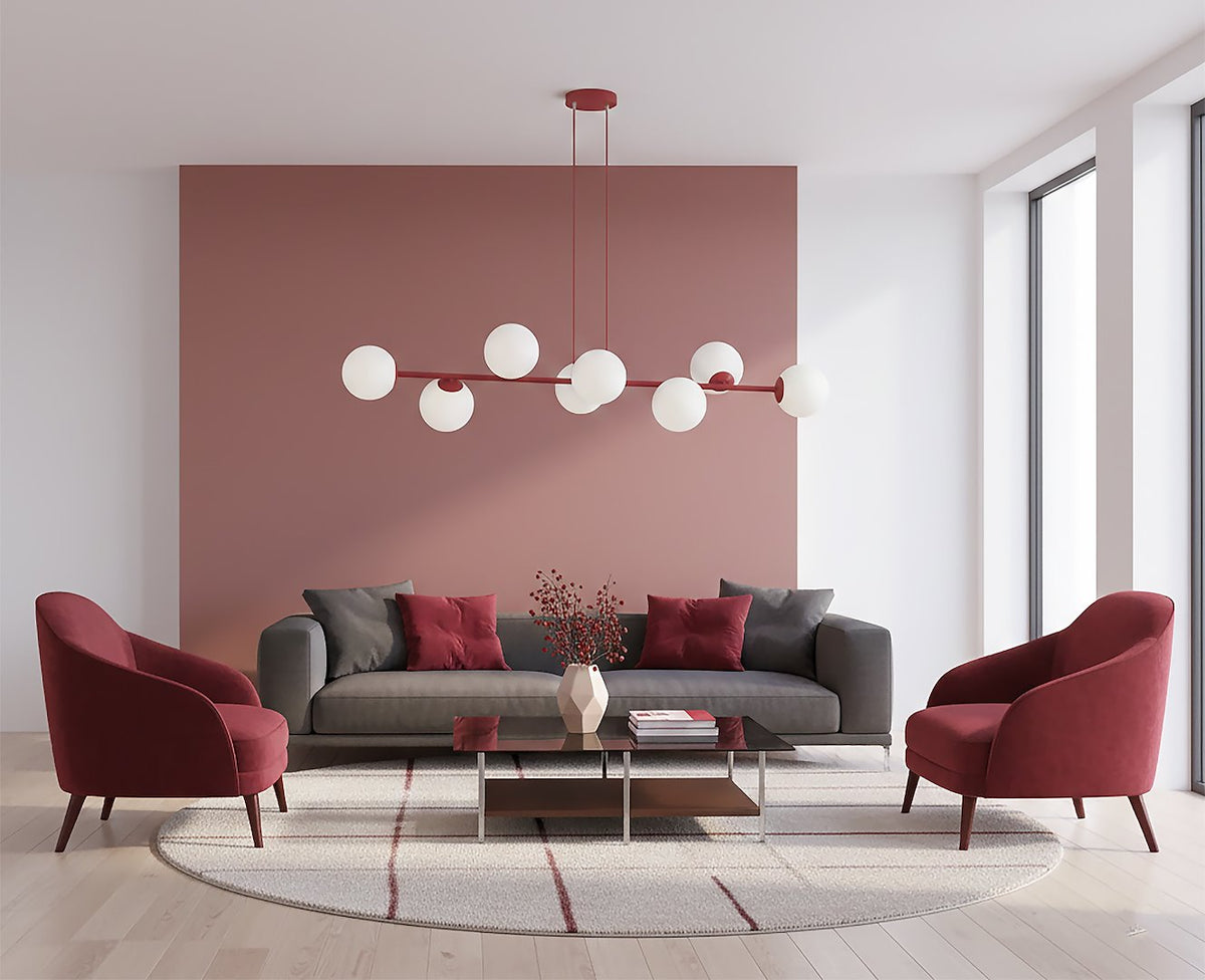 Suspension en situation dans un salon, canapé gris et fauteuils bordeaux devant un mur rose.
