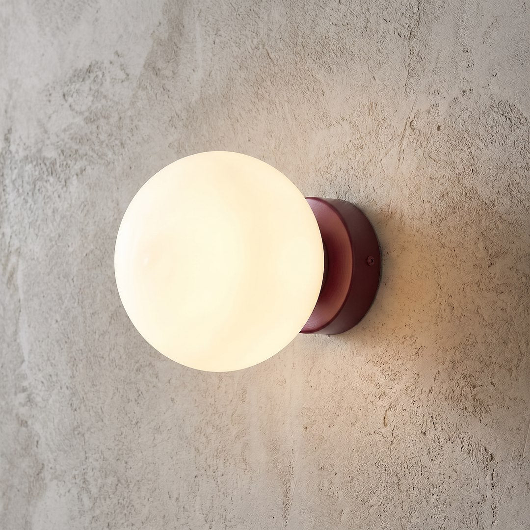 Gros plan du luminaire allumé sur un mur texturé, lumière chaude diffusée.