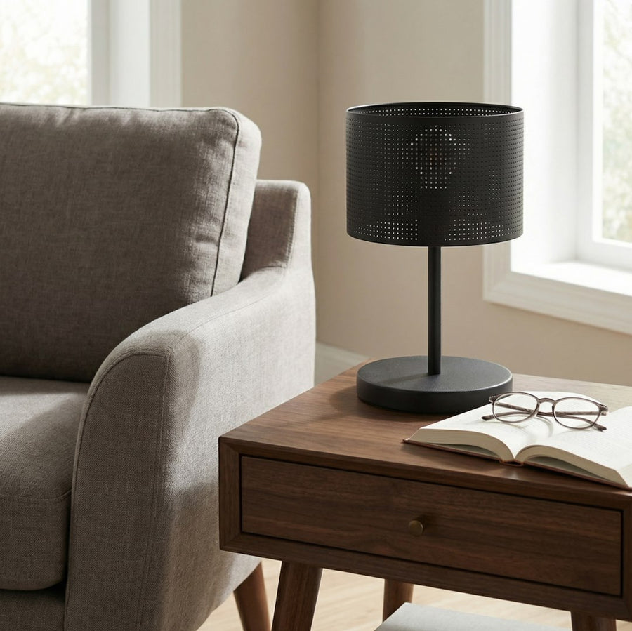 Lampe noire posée sur table de chevet en bois, près d'un fauteuil beige.