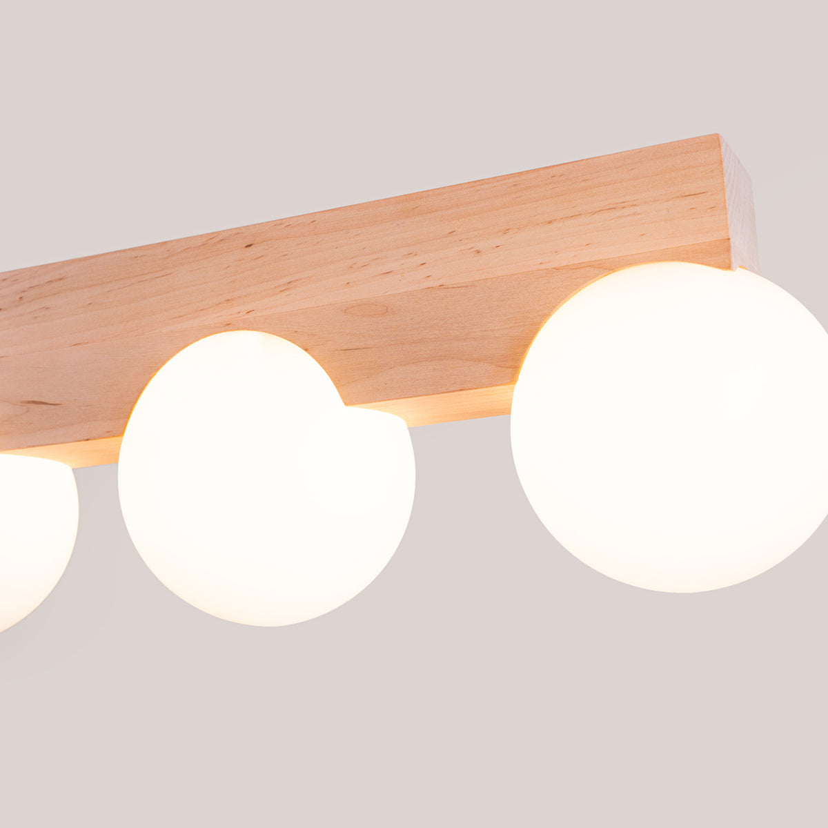 Détail rapproché du plafonnier allumé, bois et sphères lumineuses en ambiance chaude.