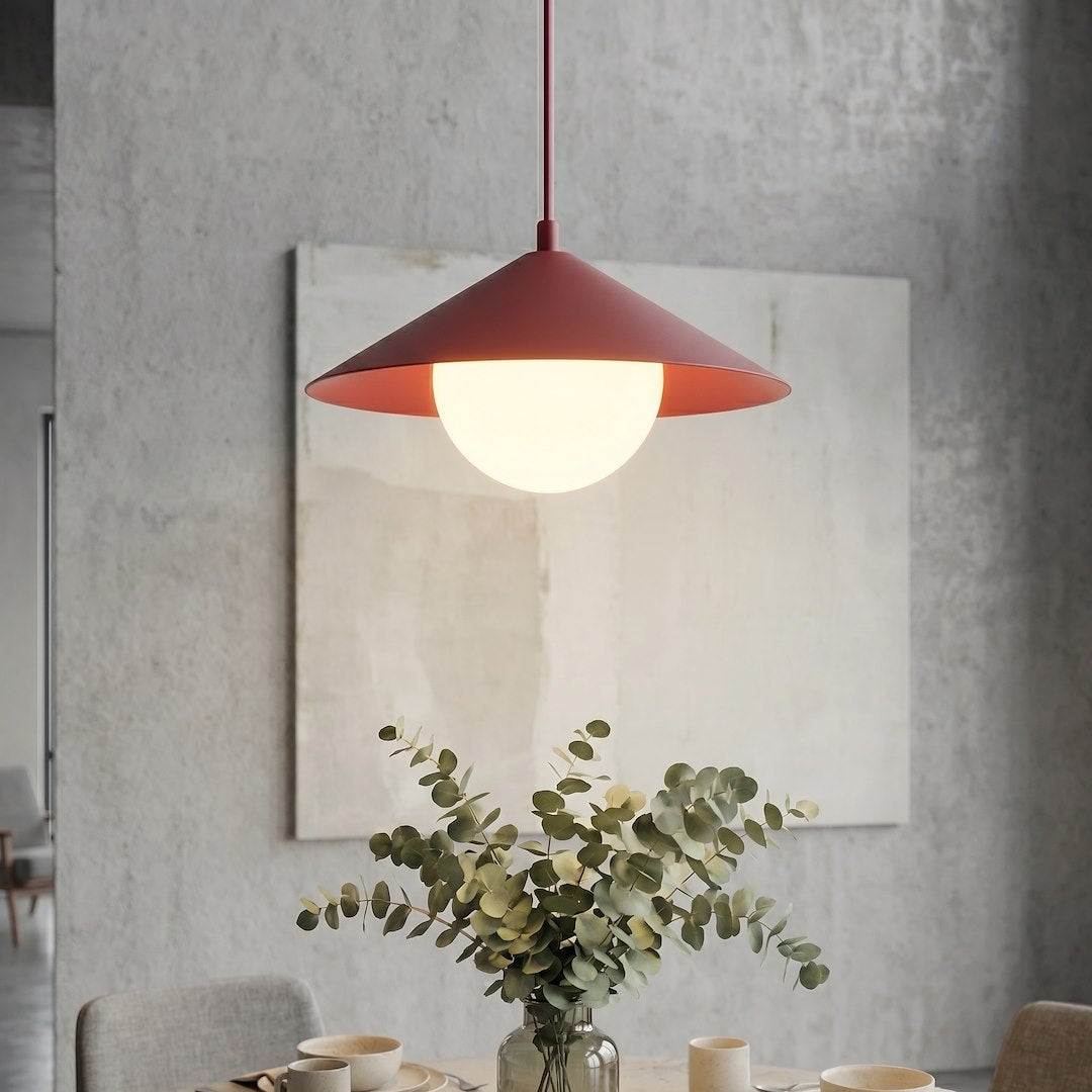 Mise en ambiance : luminaire allumé au-dessus d'une table avec vase d'eucalyptus, mur béton