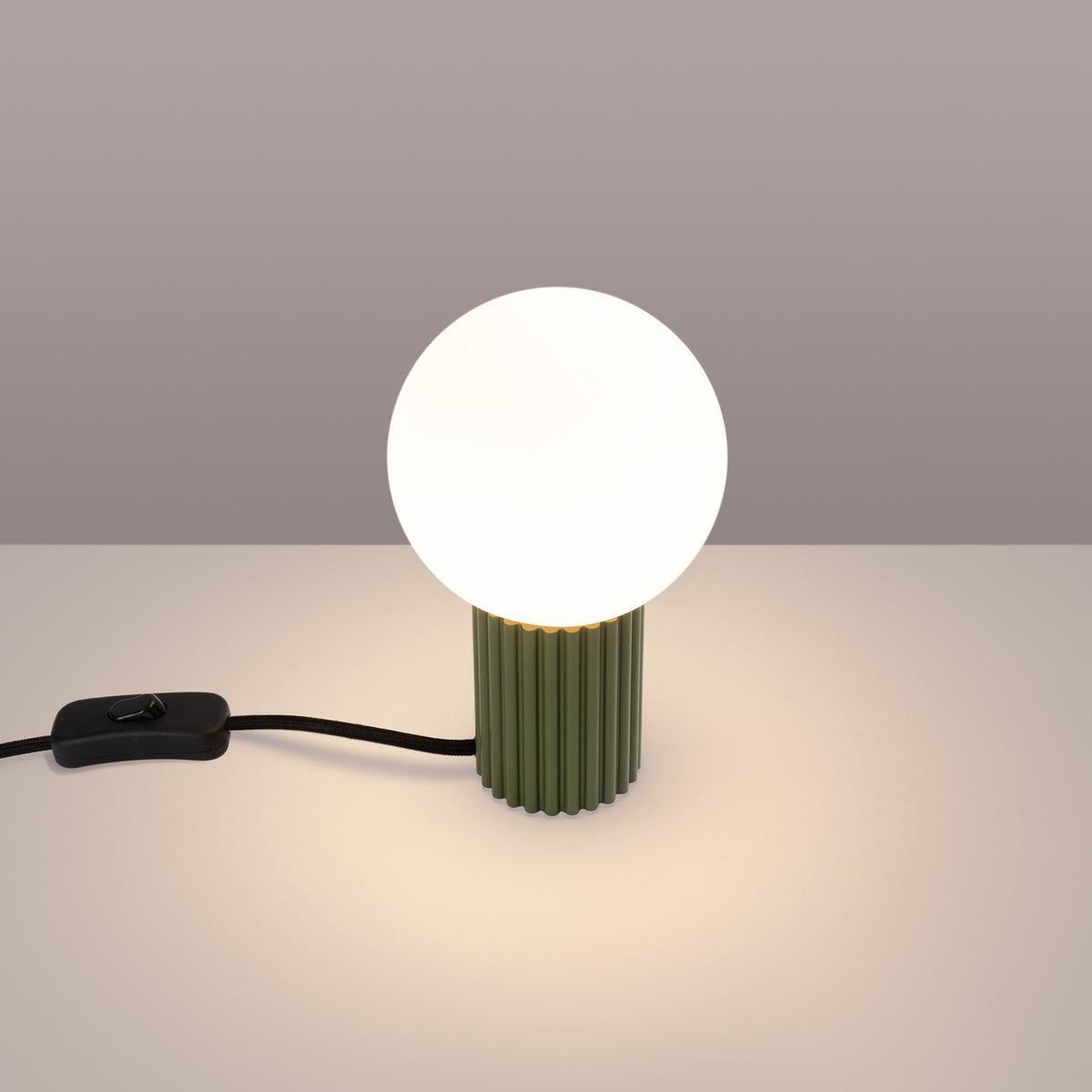Lampe verte allumée diffusant une lumière chaude sur fond gris beige.