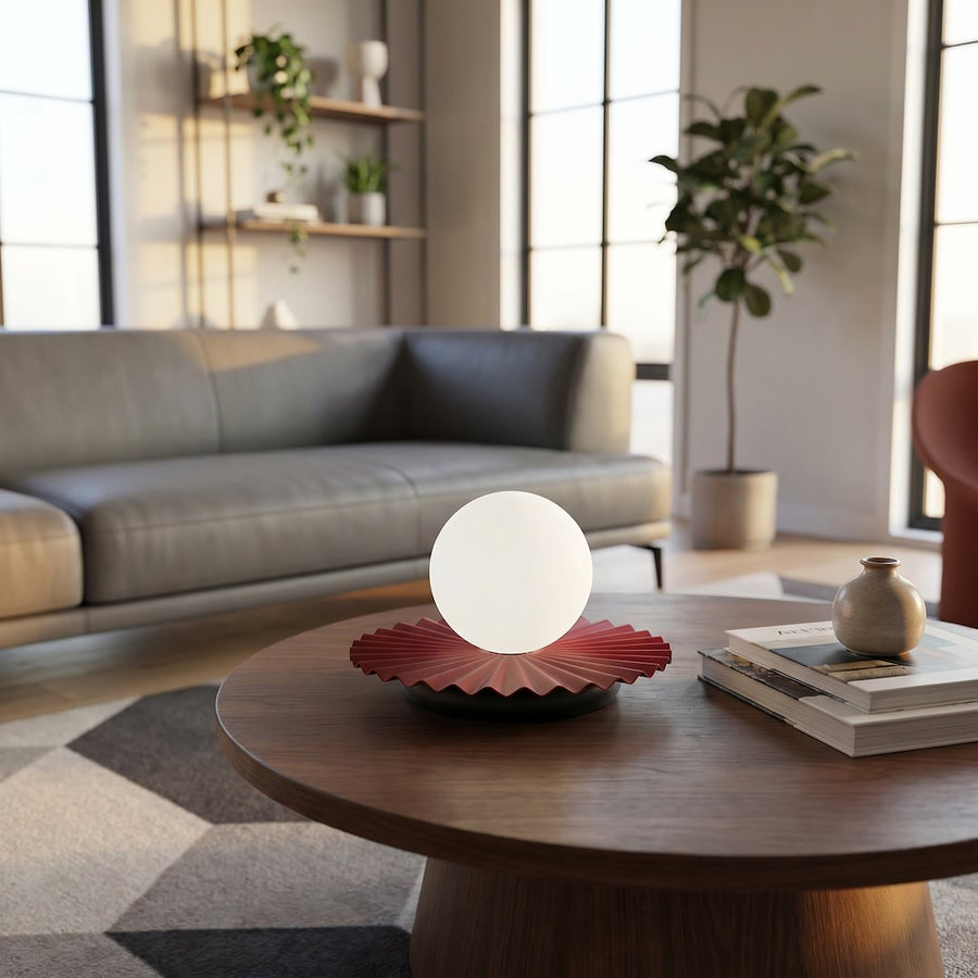 Lampe allumée sur table ronde en bois, canapé gris et fenêtres en arrière-plan