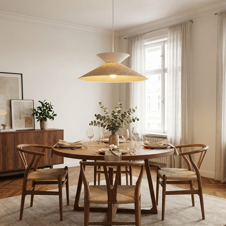 Suspension éclairée au-dessus d'une table ronde en bois, chaises et verres dressés.