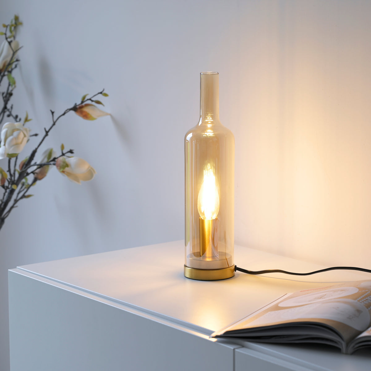 Mise en ambiance sur buffet blanc, lampe allumée près d'une branche fleurie