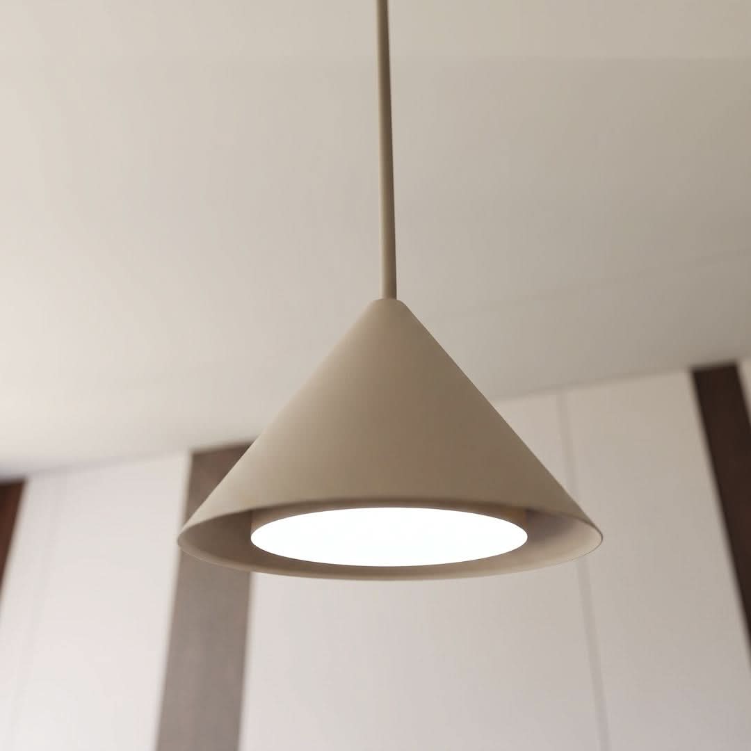 Gros plan sur un abat-jour conique beige éclairé, câble fin et plafond clair