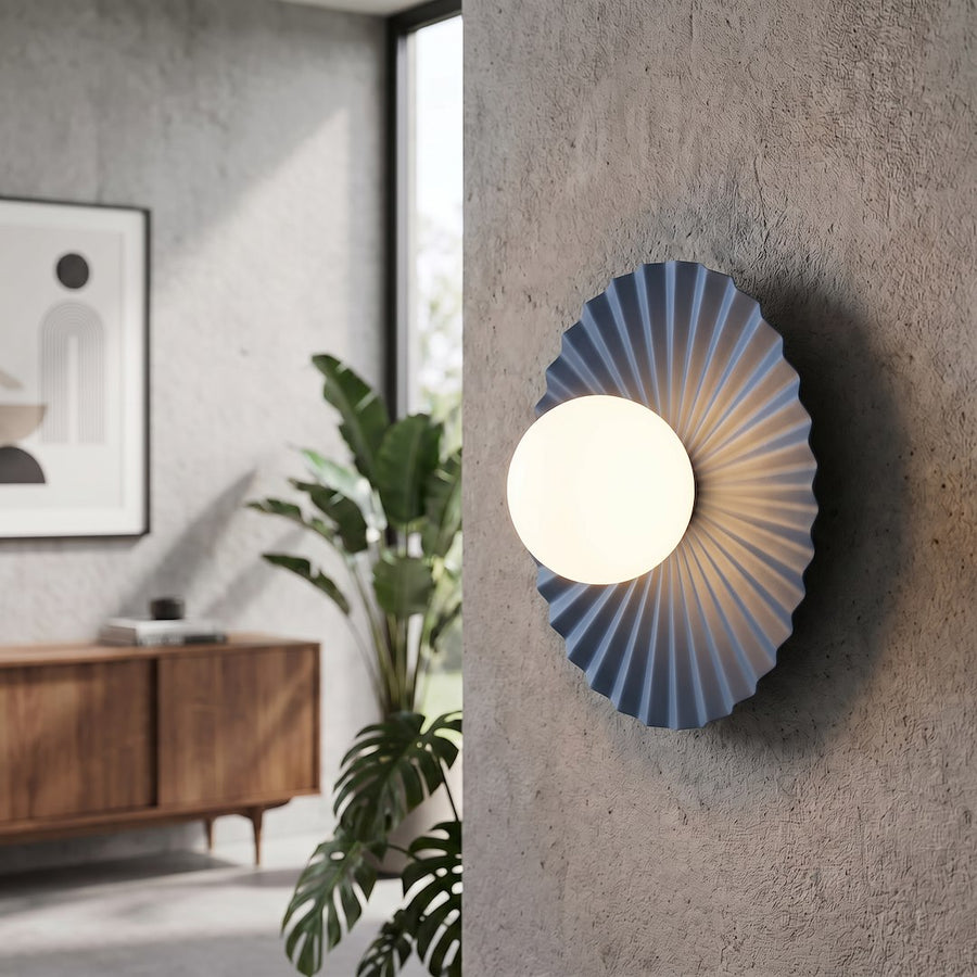 Luminaire fixé sur un mur béton gris, près d'une plante verte et d'un meuble