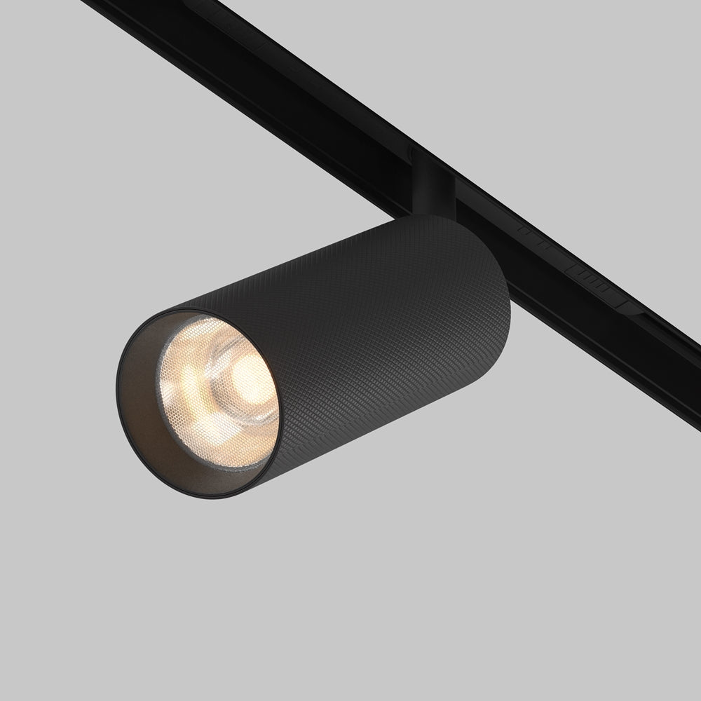 Vue rapprochée du spot cylindrique noir fixé sur rail, orienté vers le bas.
