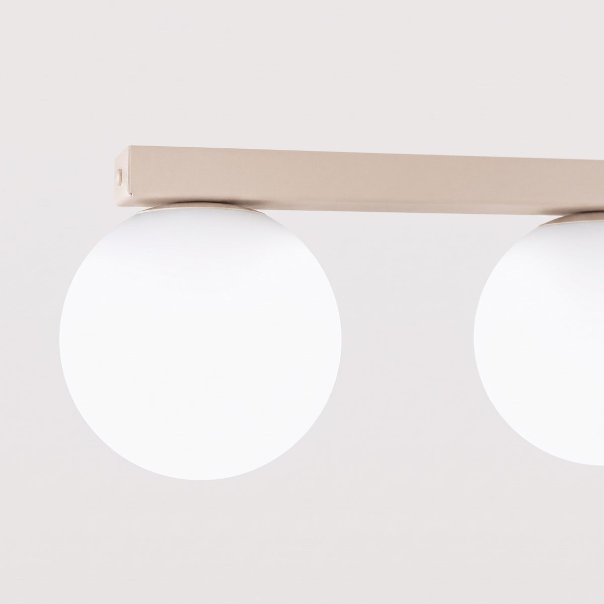 Gros plan sur deux globes blancs éteints fixés sous la barre rectangulaire beige.