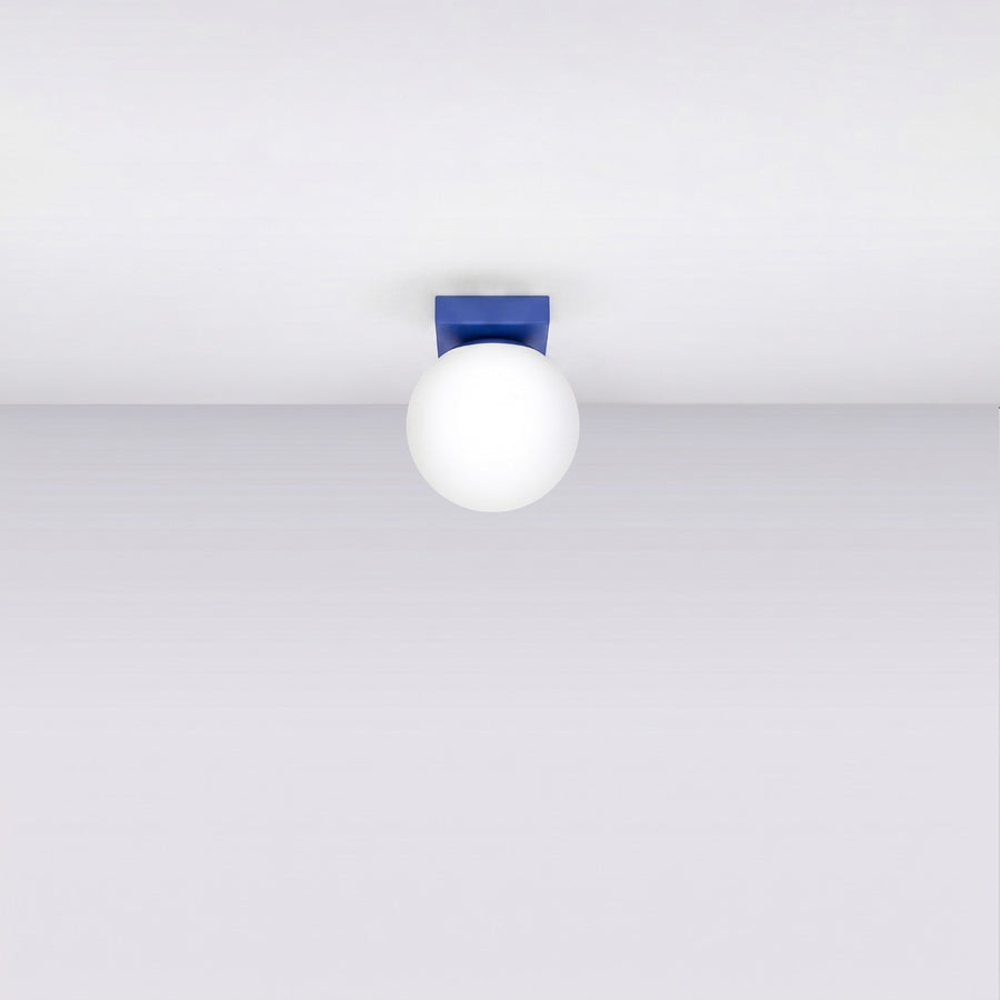 Plafonnier monté au plafond, éteint, avec socle bleu et globe blanc.
