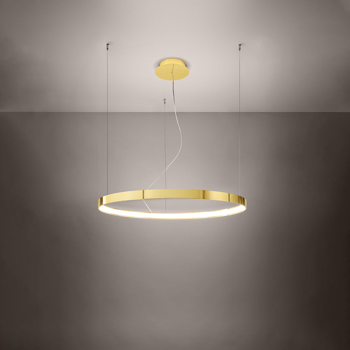 Mise en ambiance sombre montrant le lustre anneau doré diffusant une lumière chaude.