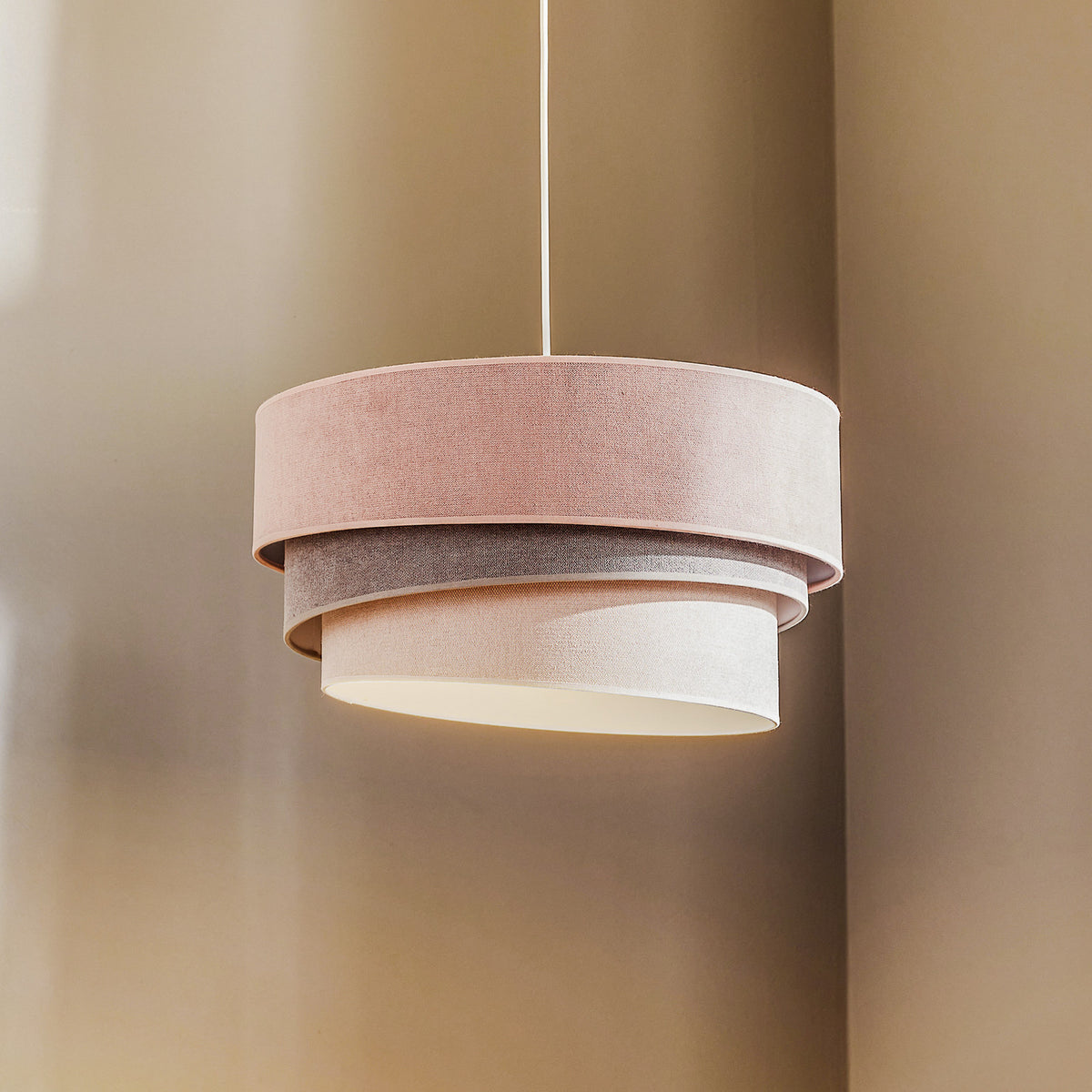 Suspension à trois abat-jours cylindriques superposés, vue de face sur fond beige.