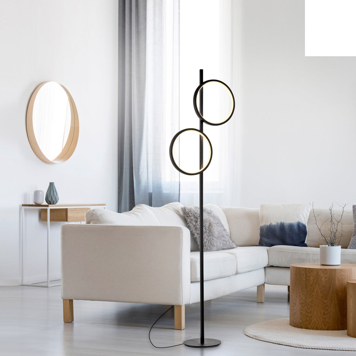 Mise en ambiance dans un salon clair, lampadaire noir allumé près du canapé.