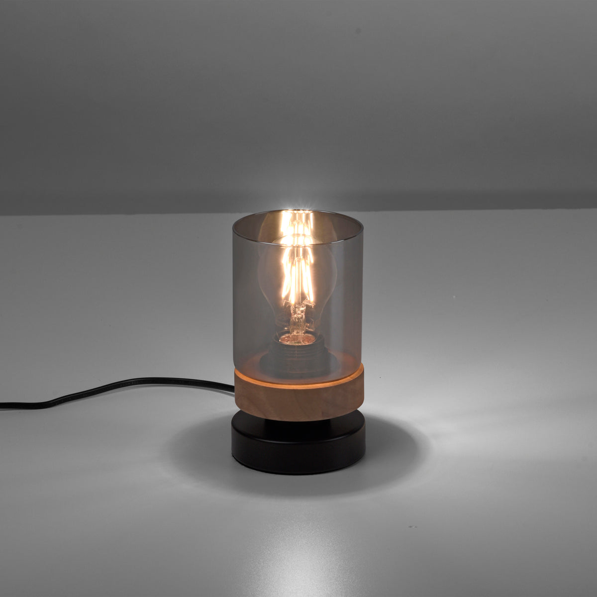 Produit allumé sur fond gris, câble noir visible et socle en bois et métal.