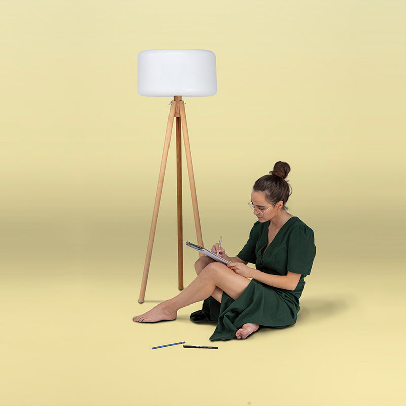 Mise en ambiance studio sur fond jaune, femme assise dessinant à côté du lampadaire