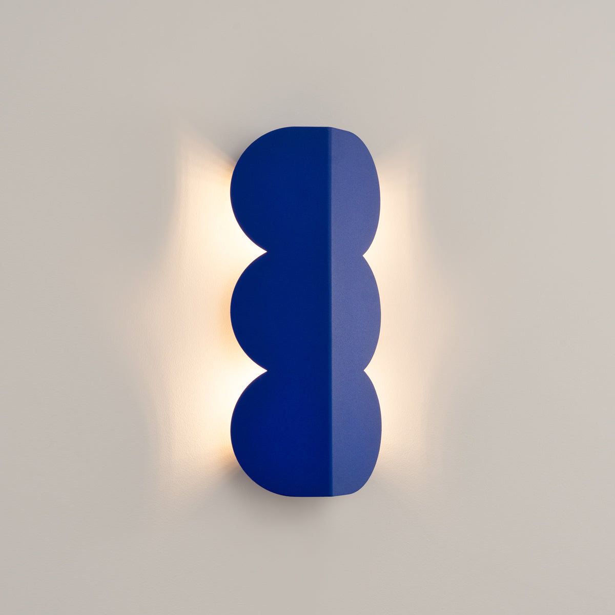 Luminaire allumé sur mur beige, halo de lumière chaude diffusée autour du produit