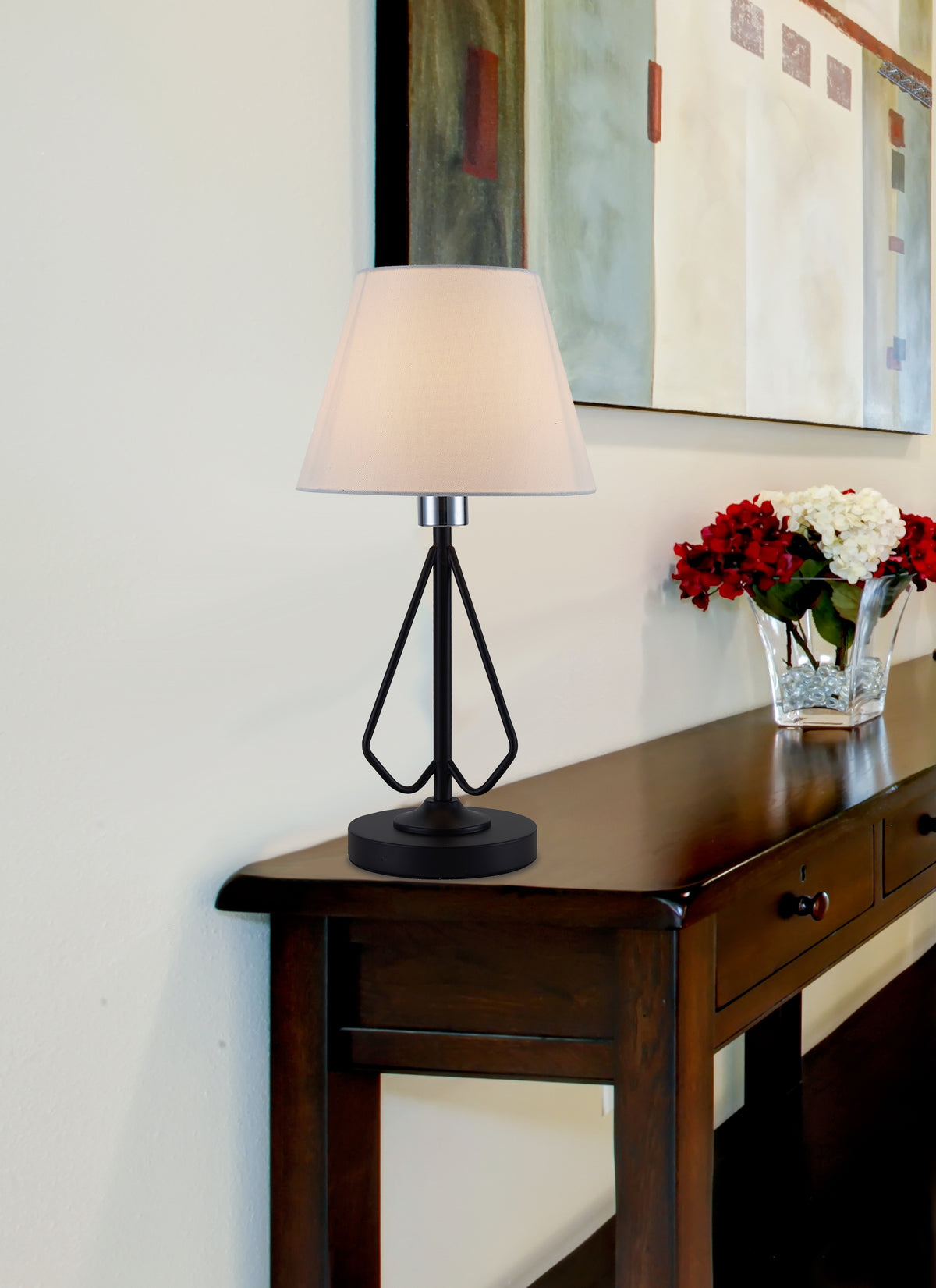 Lampe posée sur une console en bois devant un tableau et des fleurs