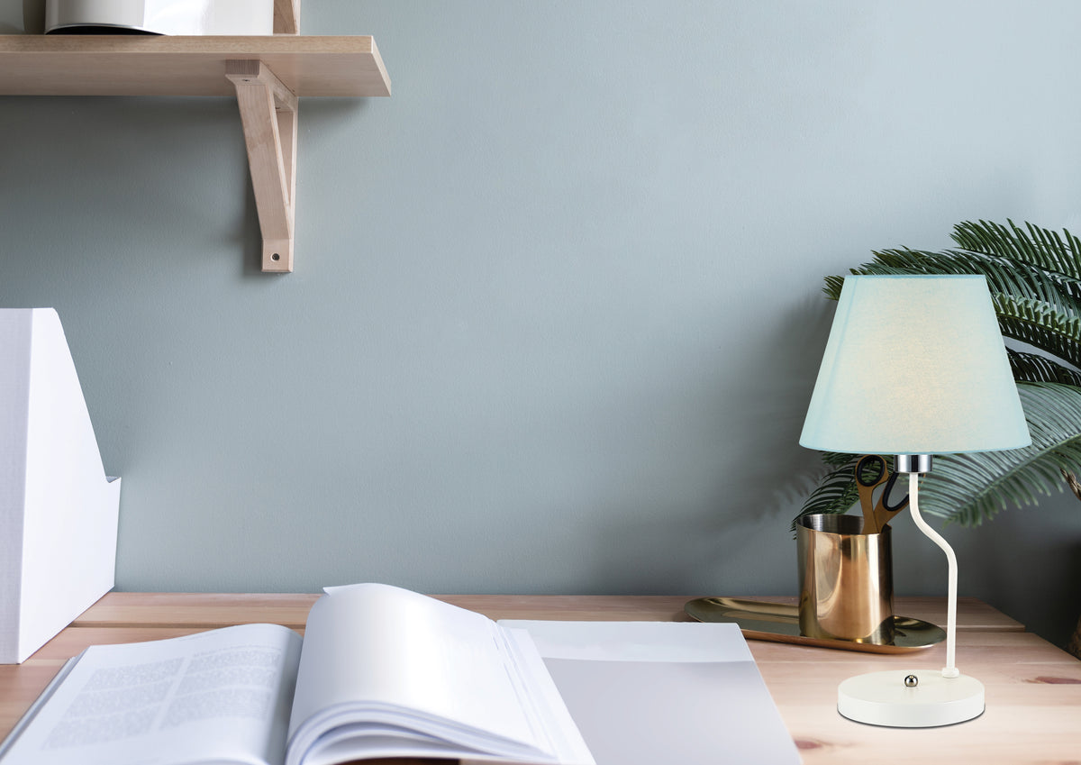 Mise en ambiance bureau : lampe blanche posée près d'un pot doré et d'une fougère