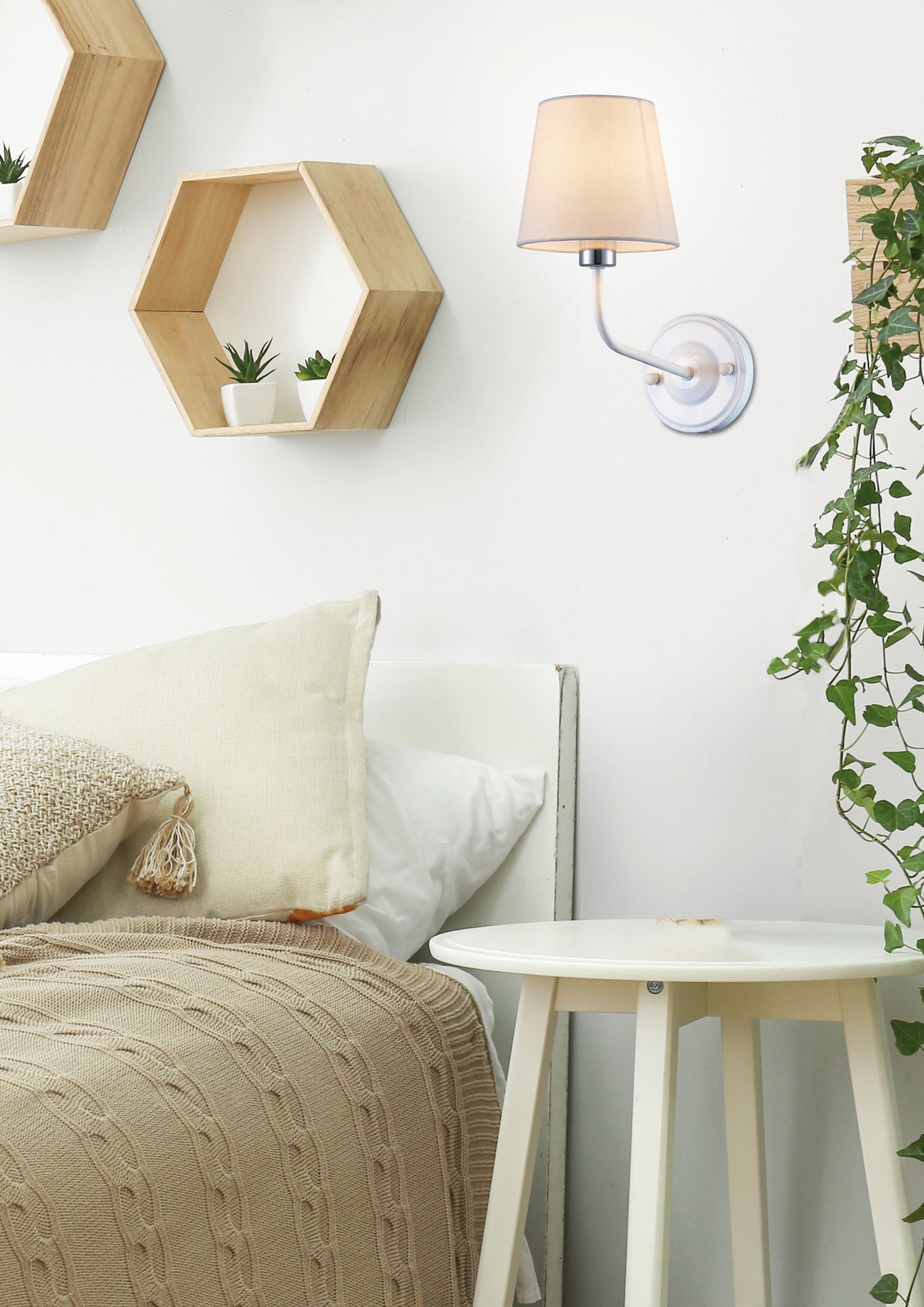 Mise en ambiance chambre : applique allumée près du lit, étagères hexagonales et plantes.