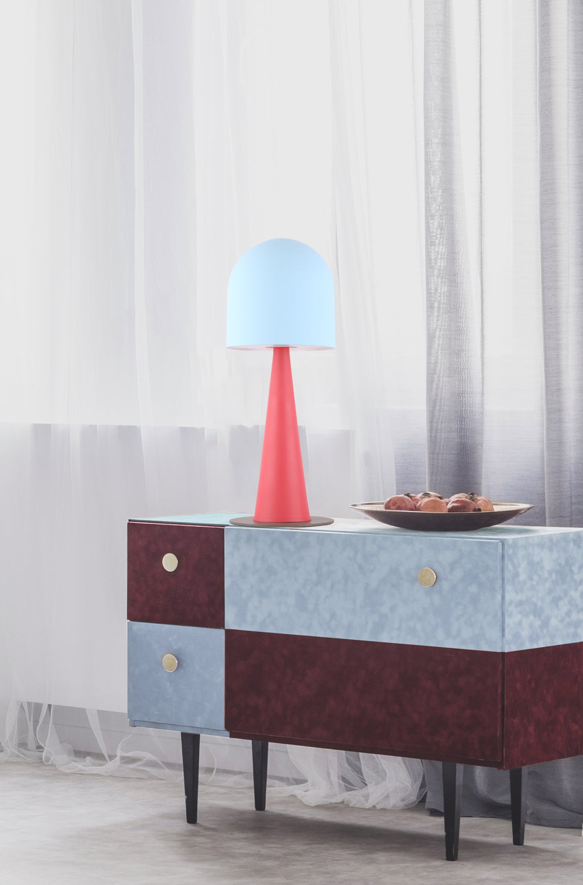 Lampe rose allumée posée sur une commode devant des rideaux blancs, mise en ambiance intérieure