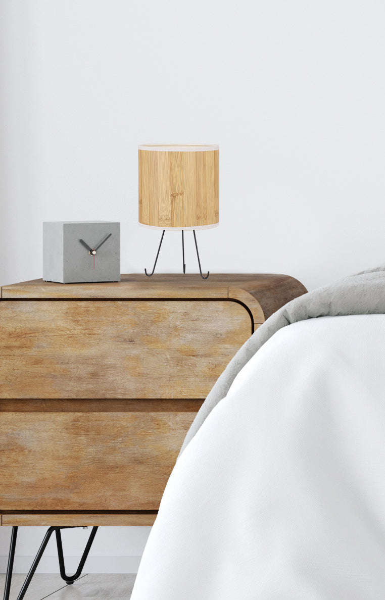 Mise en ambiance sur une commode en bois, lampe éteinte près d'un réveil gris.