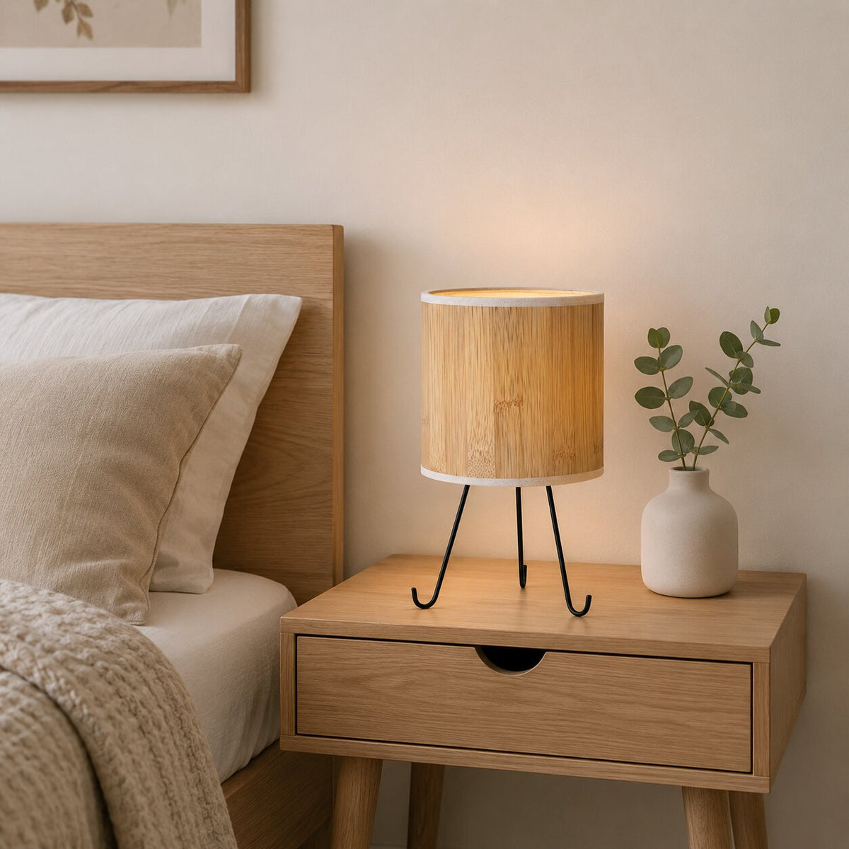 Lampe allumée sur une table de chevet en chêne, lumière chaude et vase avec eucalyptus.