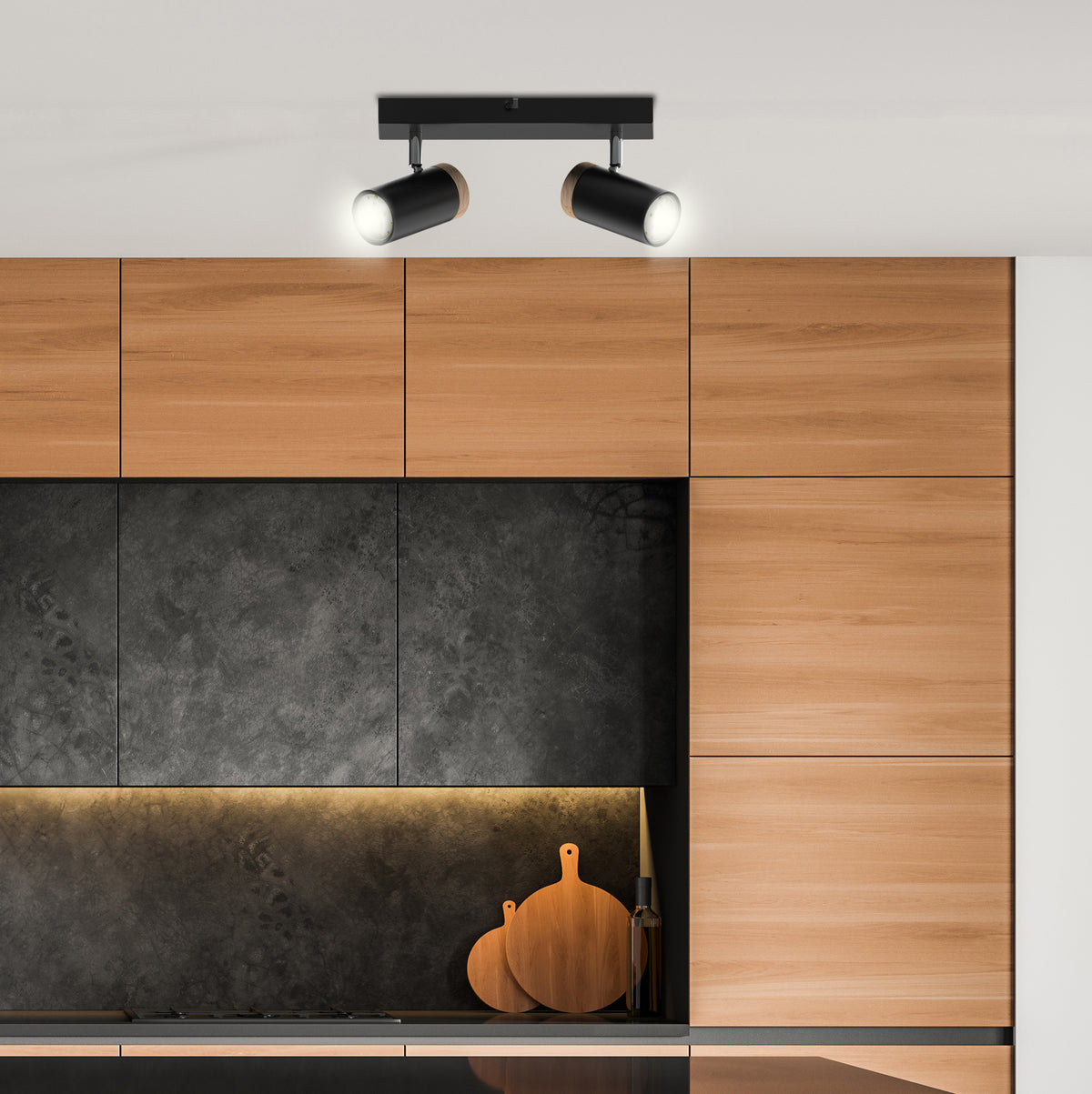 Mise en ambiance cuisine moderne, spots allumés au-dessus des meubles en bois et crédence sombre
